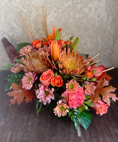 Harvest Abundance Cornucopia featuring orange roses, orange carnations, bronze spider mums, and fall accents in a wicker cornucopia.