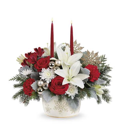 Winter Wishes Bouquet with red roses, white lilies, carnations, winter greens, and two candles in a snowflake dish.