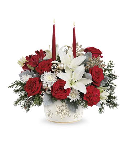 Winter Wishes Bouquet with red roses, white lilies, carnations, winter greens, and two candles in a snowflake dish.