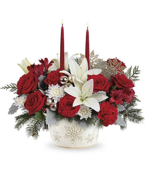 Winter Wishes Bouquet with red roses, white lilies, carnations, winter greens, and two candles in a snowflake dish.